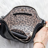 Black handbag with floral interior lining held by a person on a white background