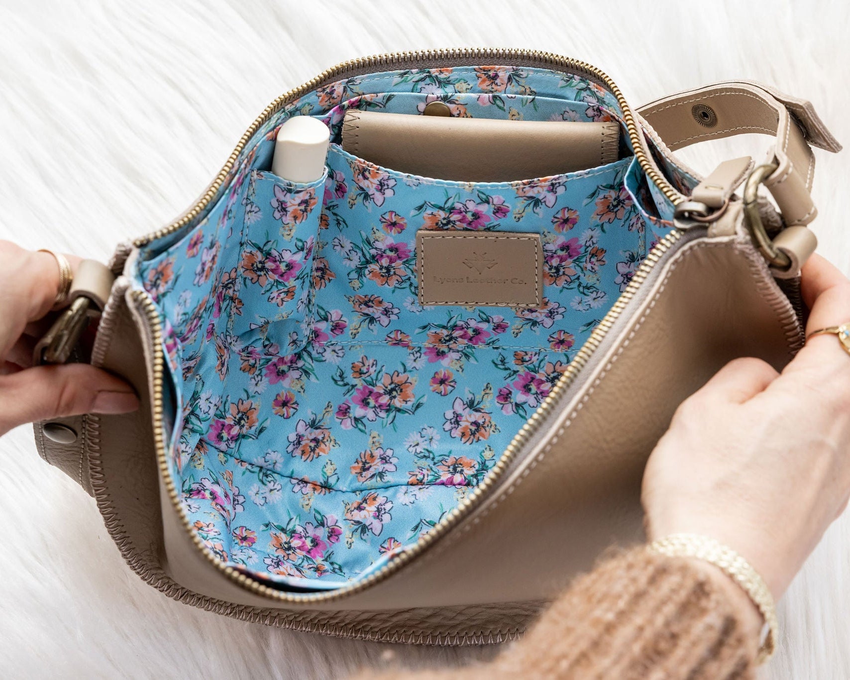 Handbag with floral interior being held open by a person's hands on a light background