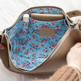 Handbag with floral interior being held open by a person's hands on a light background