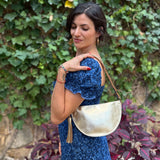 Woman in a blue dress holding a gold handbag against a green ivy wall.