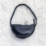 Black leather bag with a phone inside on a white fluffy surface