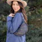 Woman wearing a blue jacket and beige hat with a round patterned bag, standing outdoors.