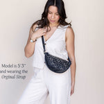Woman wearing a white outfit with a black patterned bag on a plain background