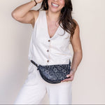 Woman wearing a white sleeveless top and pants with a leopard print fanny pack against a plain background