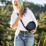 Woman holding a black bag outdoors with greenery in the background