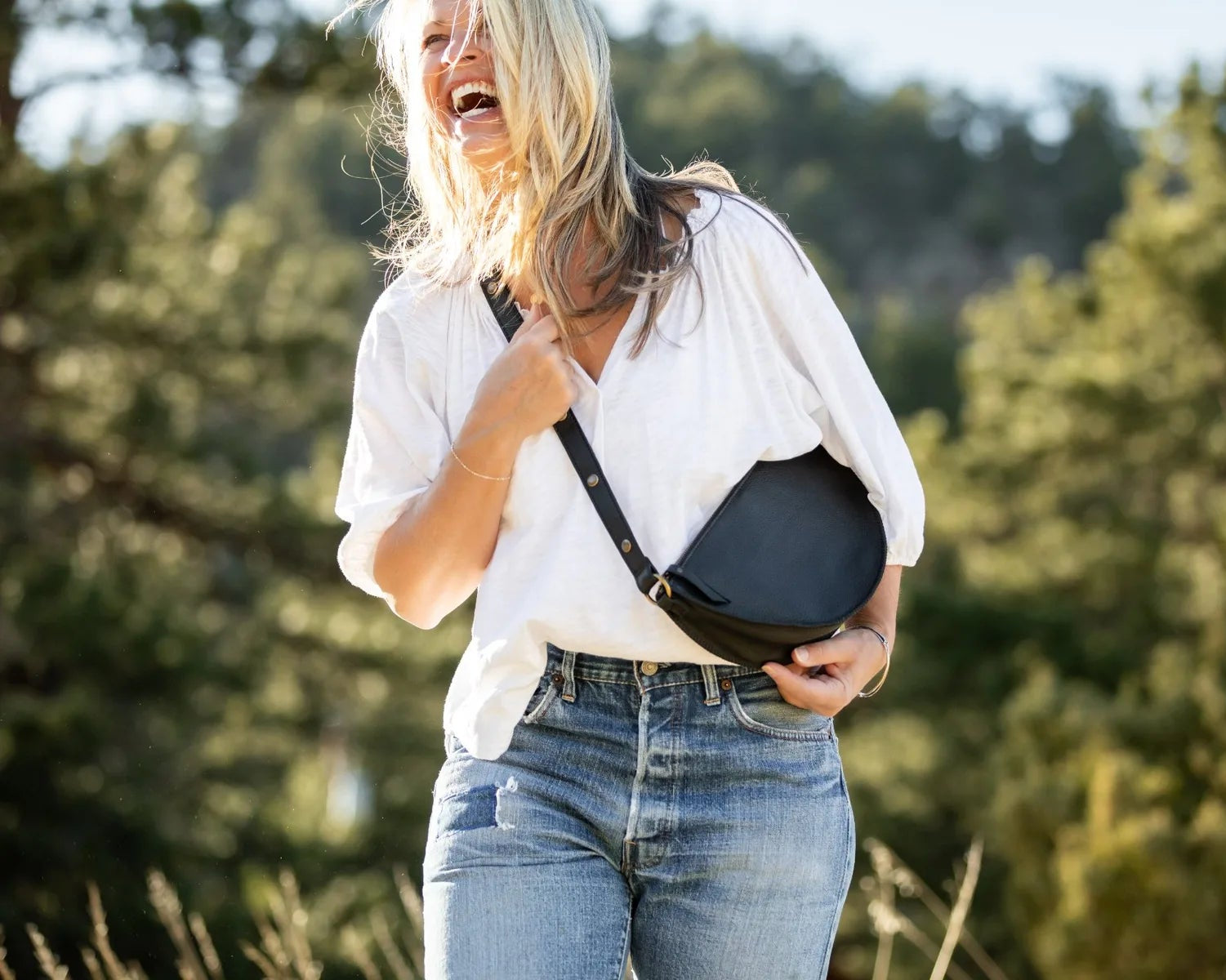 Woman holding a black bag outdoors with greenery in the background