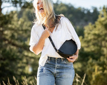 Woman holding a black bag outdoors with greenery in the background