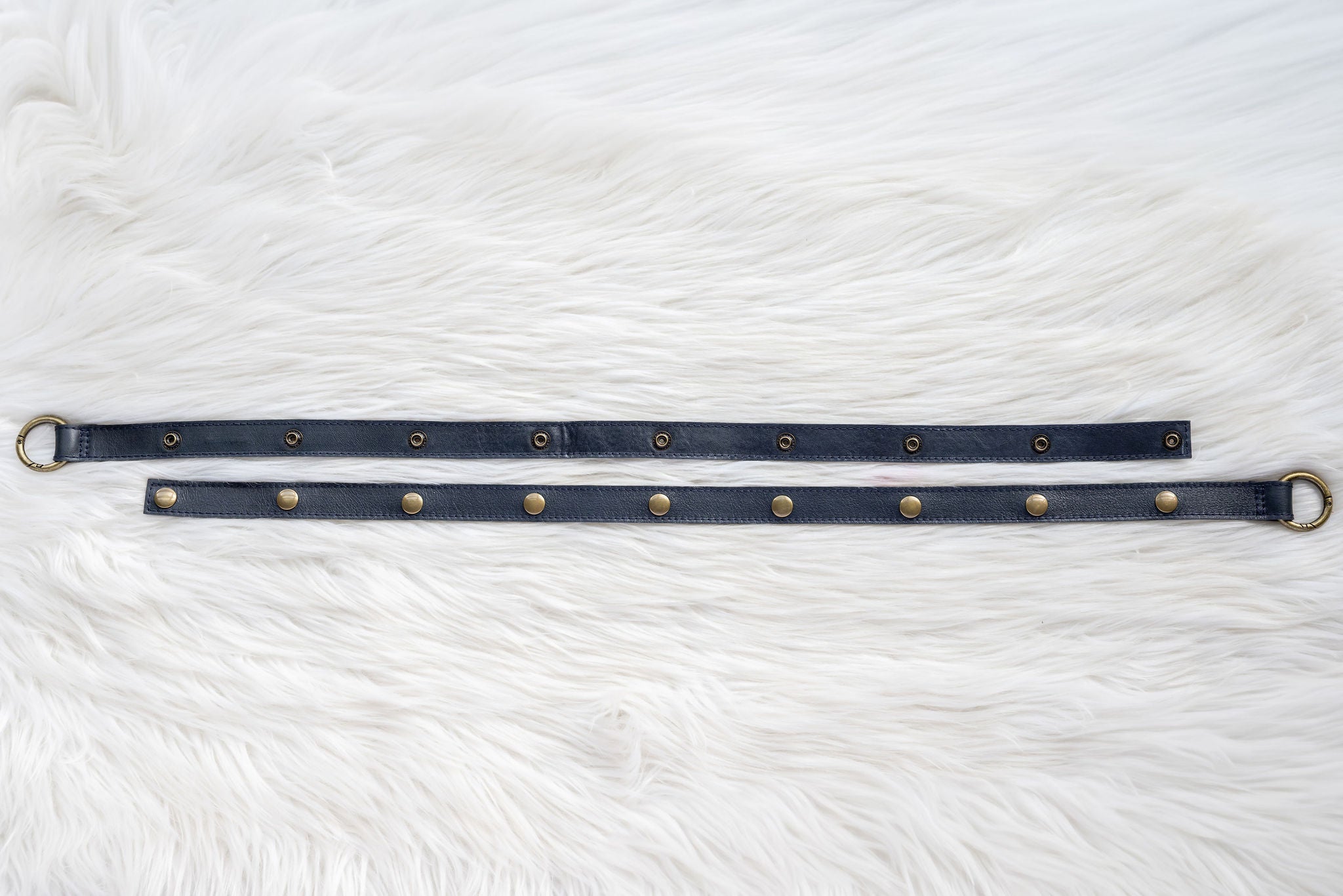 Navy leather straps with gold snaps on a white fur background